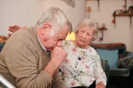 Senior woman looking concerned while her husband is coughing, possibly choking