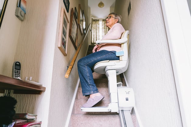 senior-woman-using-automatic-stairlift-on-a-stairc-2022-11-15-17-04-10-utc